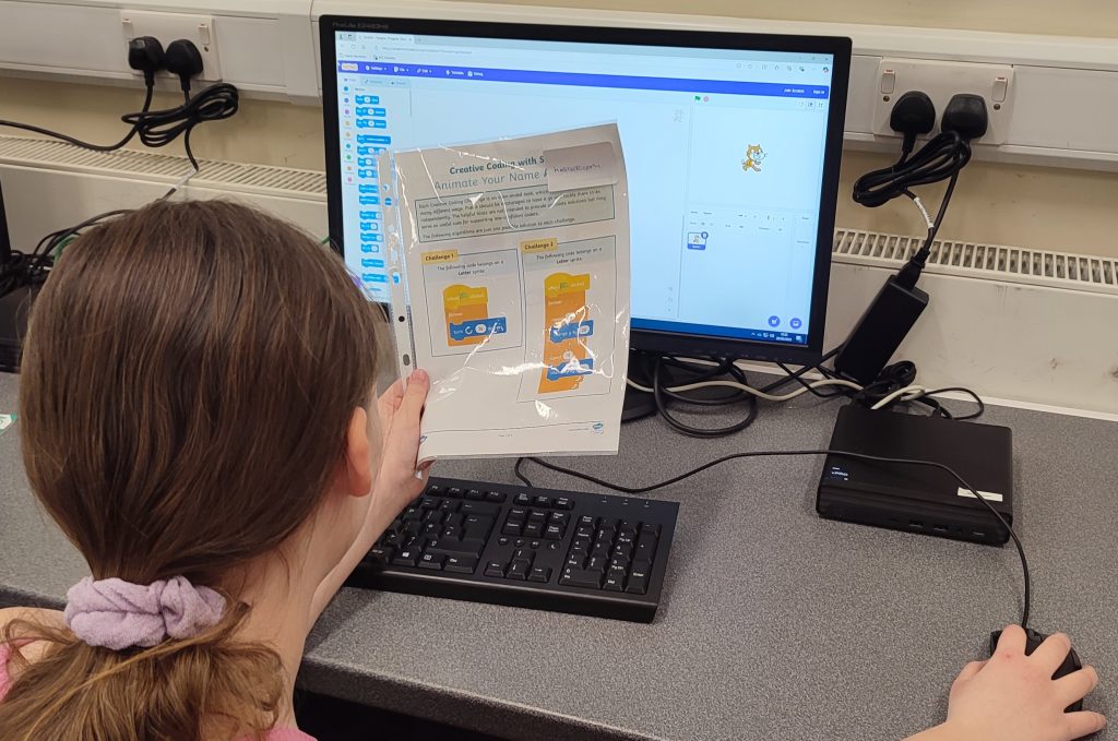 Child at Computer holding a laminated piece of paper with instructions