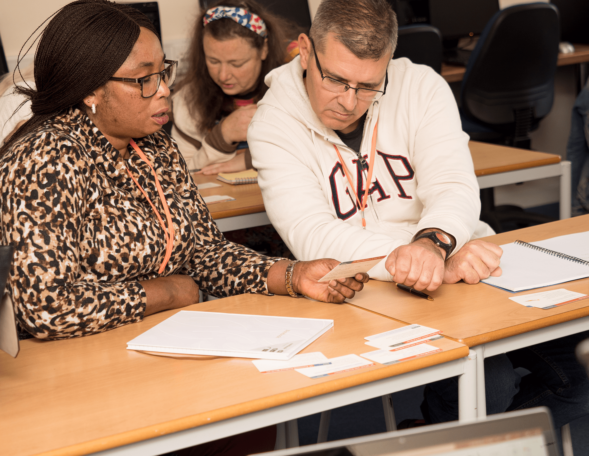 Two adult learners at a desk talking about work on the table